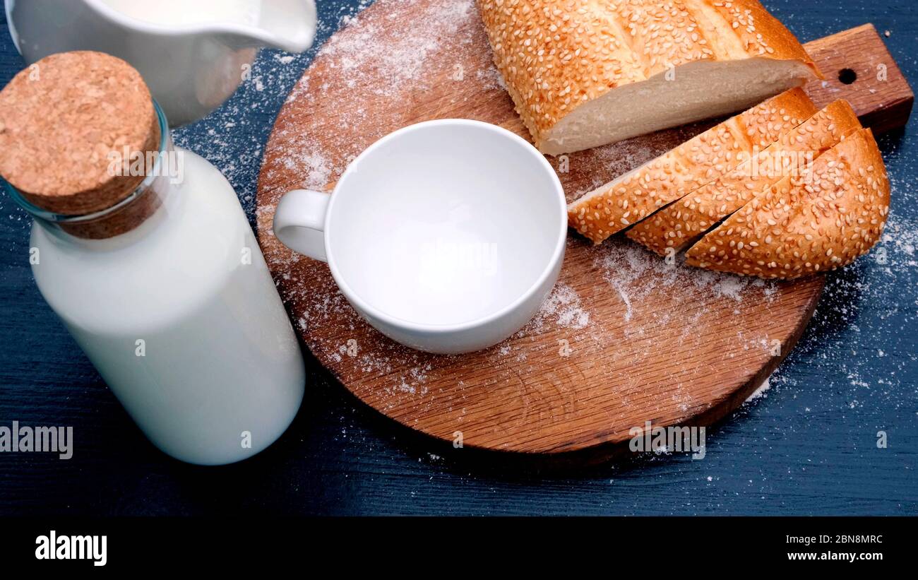Primo piano di latte versato in una tazza bianca su sfondo di legno accanto al pane. Foto Stock