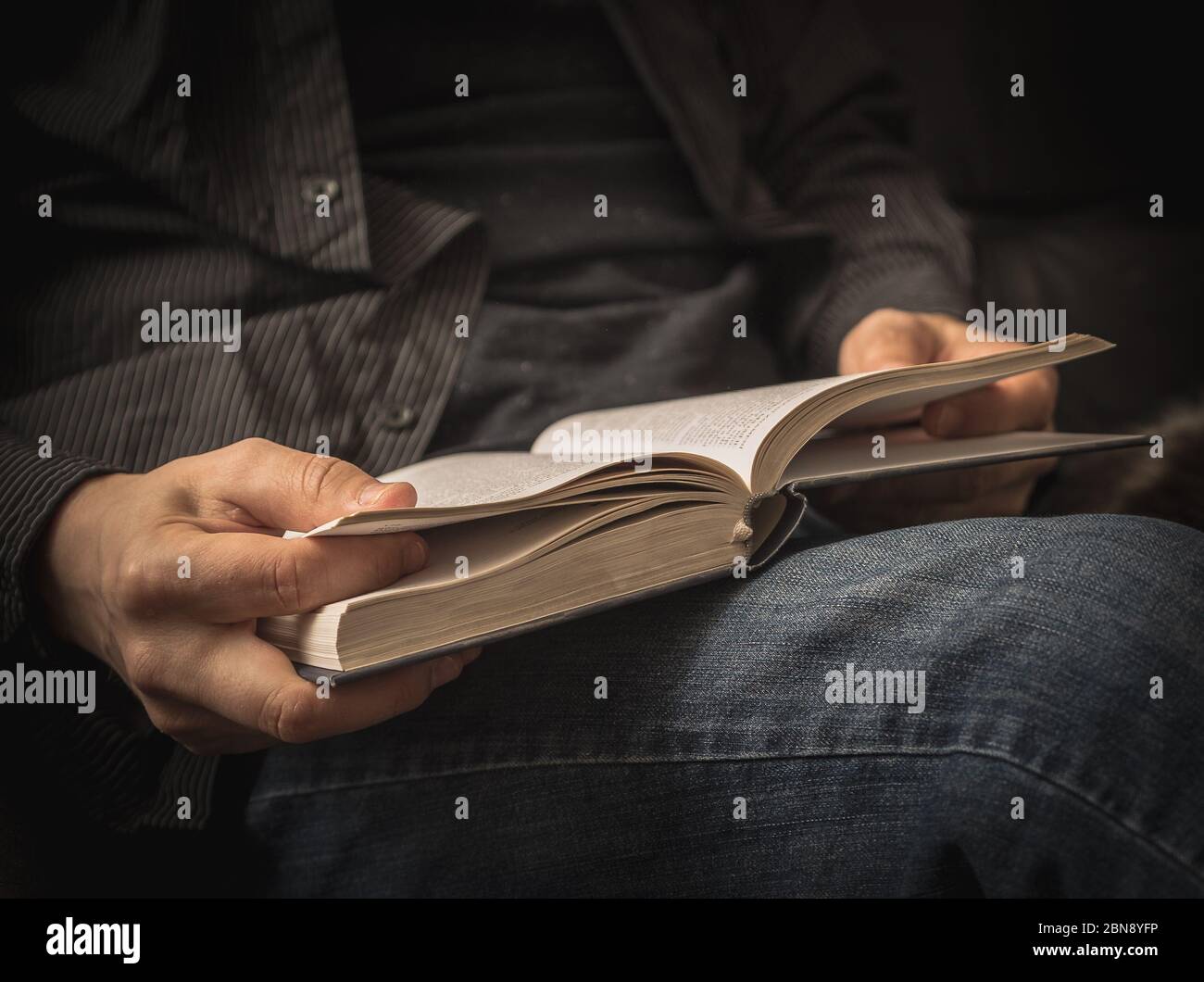 Libro di lettura con camicia nera sul divano. Foto Stock