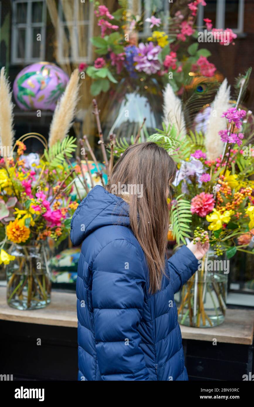 Giovane donna sorridente che seleziona fiori freschi di fronte al negozio di fiori esporre Foto Stock