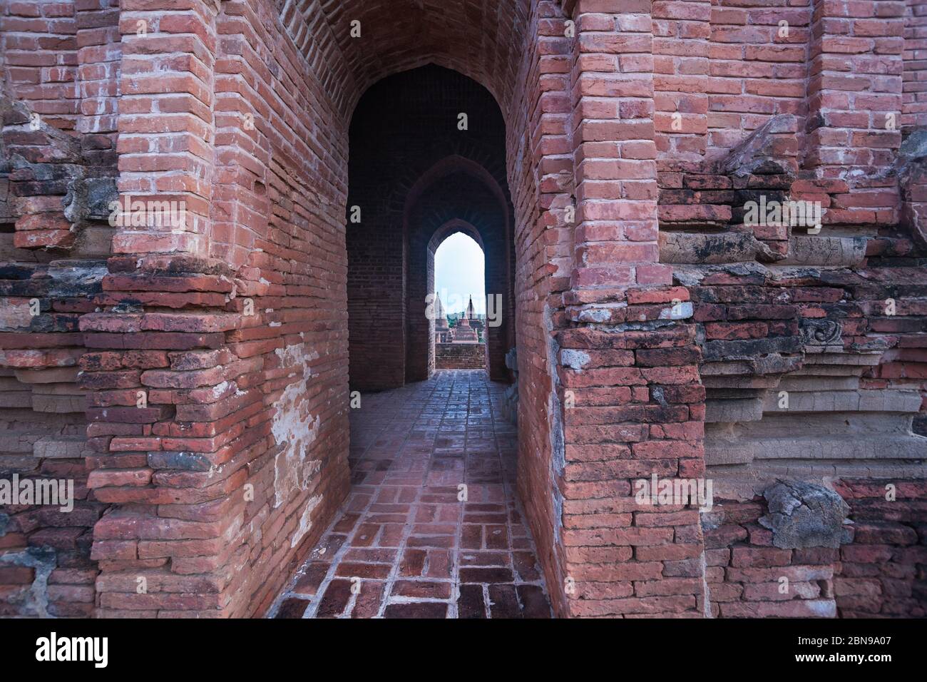 Myanmar viaggio immagini di templi distanti e stupa visto attraverso lungo arco di mattoni rossi corridoio di costruzione in declino. Foto Stock