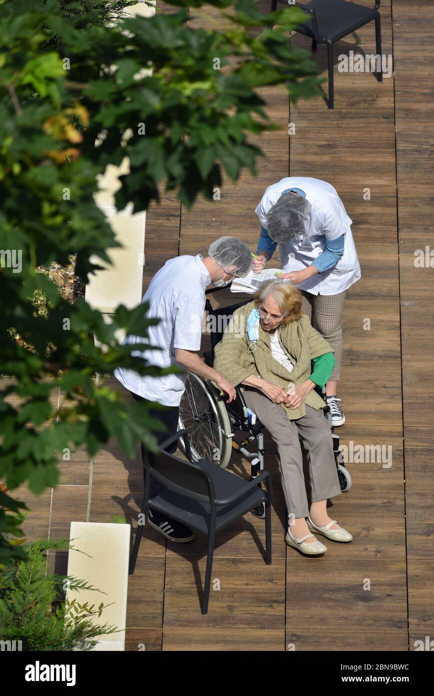 Infermieri che si prendono cura di una donna anziana e disabile in una casa di cura in una giornata di sole durante la pandemia del coronavirus Covid-19. Gli accompagnatori indossano una maschera facciale. Foto Stock