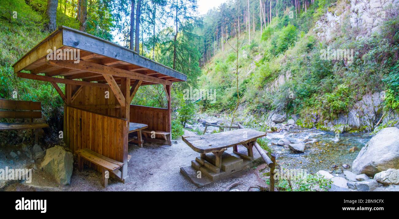 panca di legno per riposarsi escursionisti e ammirare le alte montagne con laghi limpidi, prati verdi e foreste lussureggianti e rocce taglienti sotto il cielo blu Foto Stock