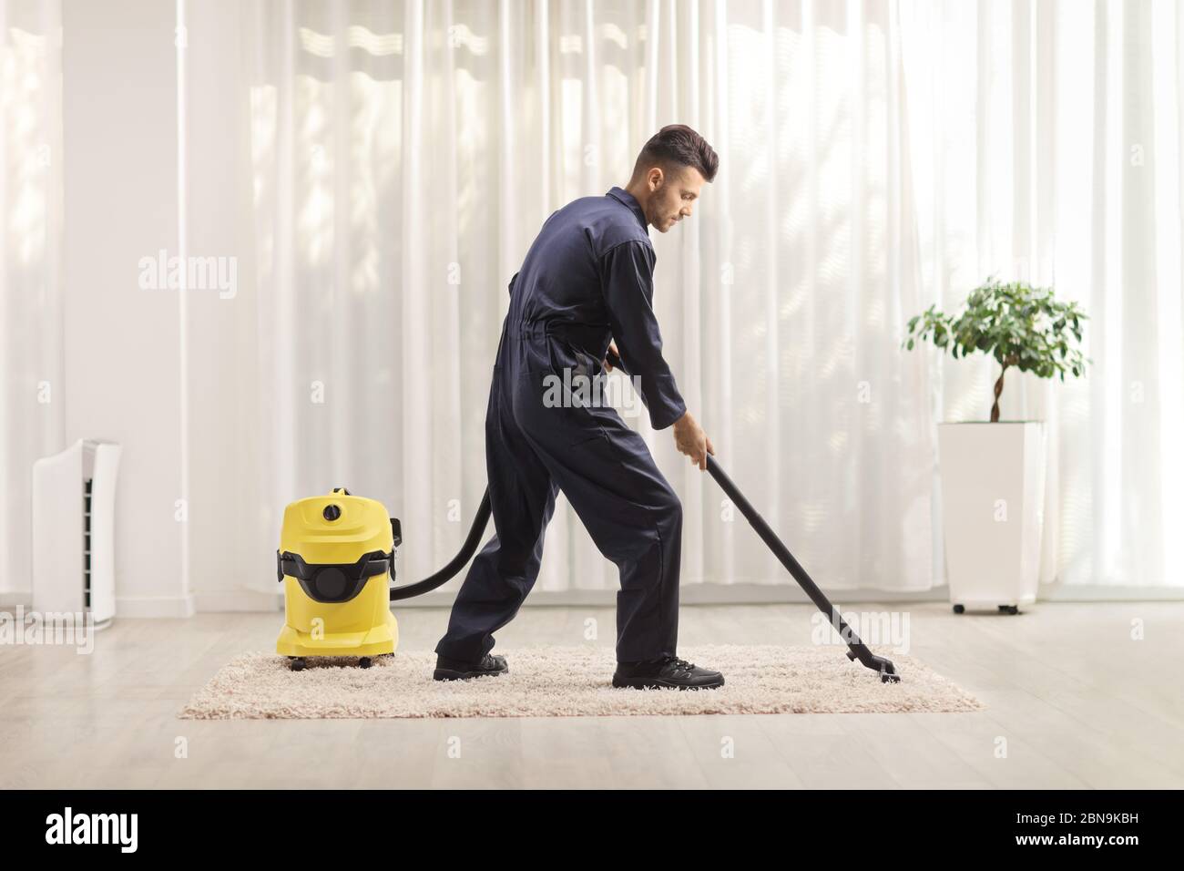 Scatto a tutta lunghezza di un uomo in uniforme che aspira un tappeto in una casa Foto Stock