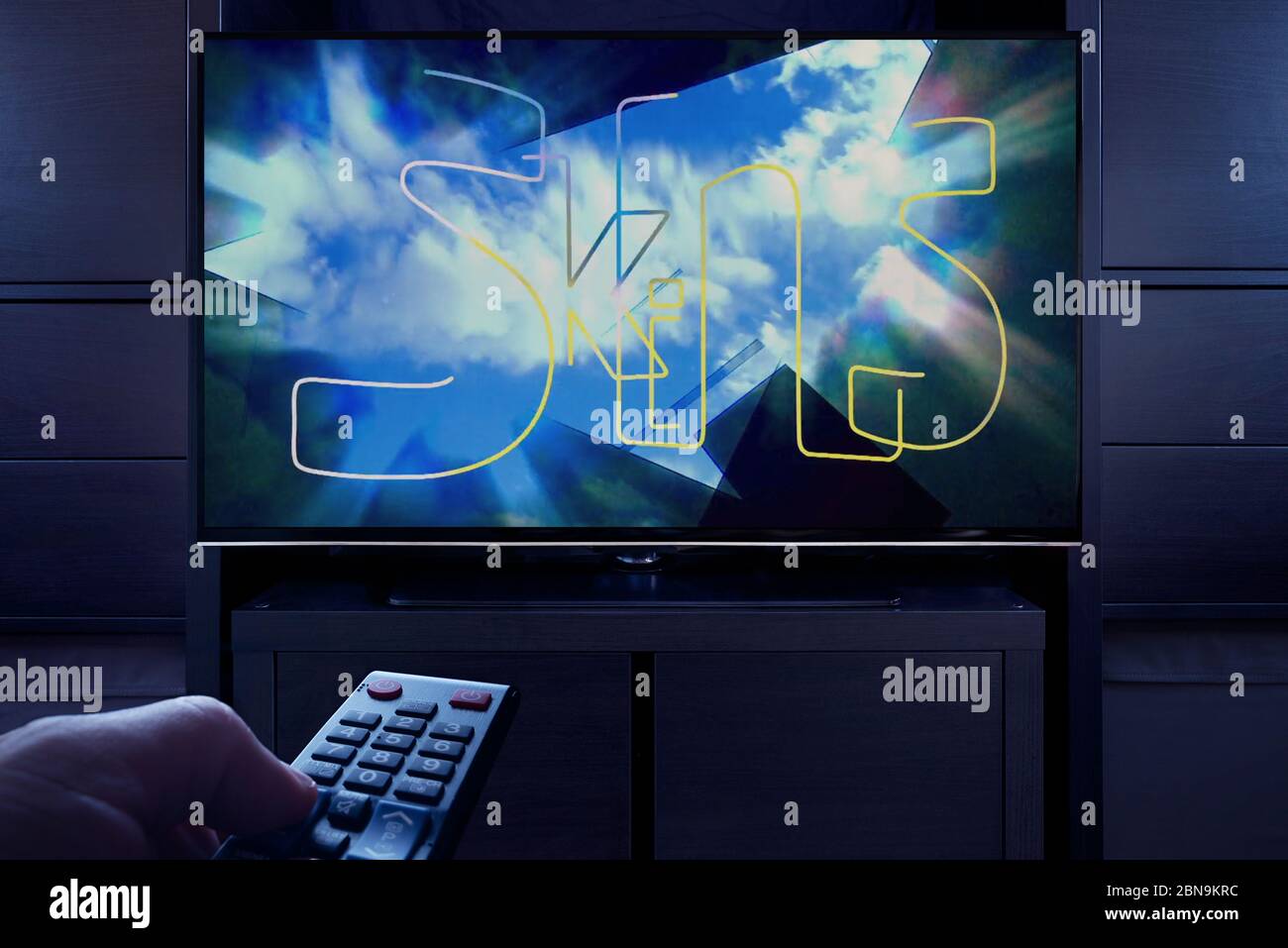 Un uomo punta un telecomando TV verso il televisore che visualizza la schermata principale del titolo Skins (solo per uso editoriale). Foto Stock