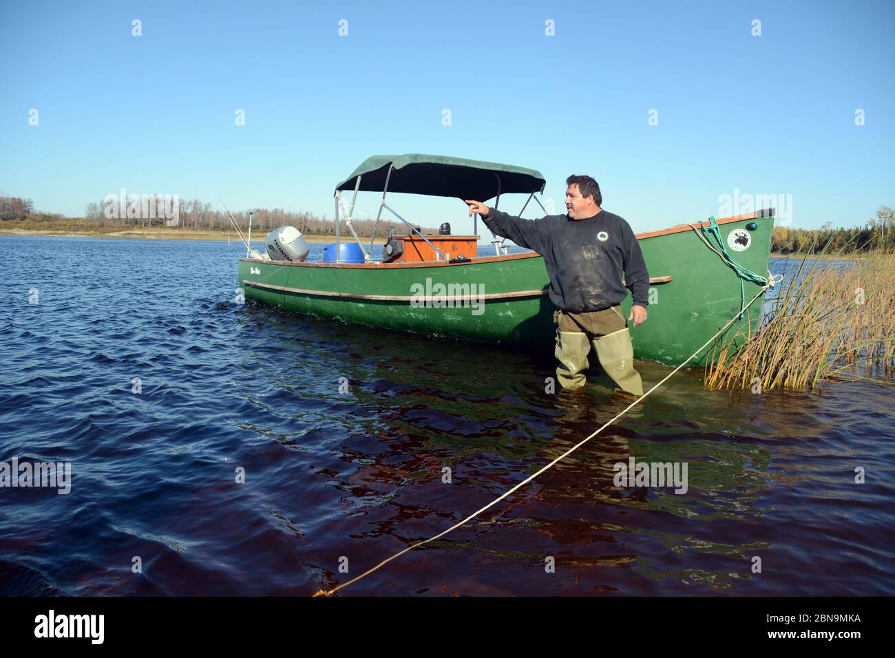 Un uomo indigeno Ojibwe si trova accanto alla sua barca e punta a una posizione lontana nel fiume Moose vicino alla città di Moose Factory, Ontario, Canada. Foto Stock