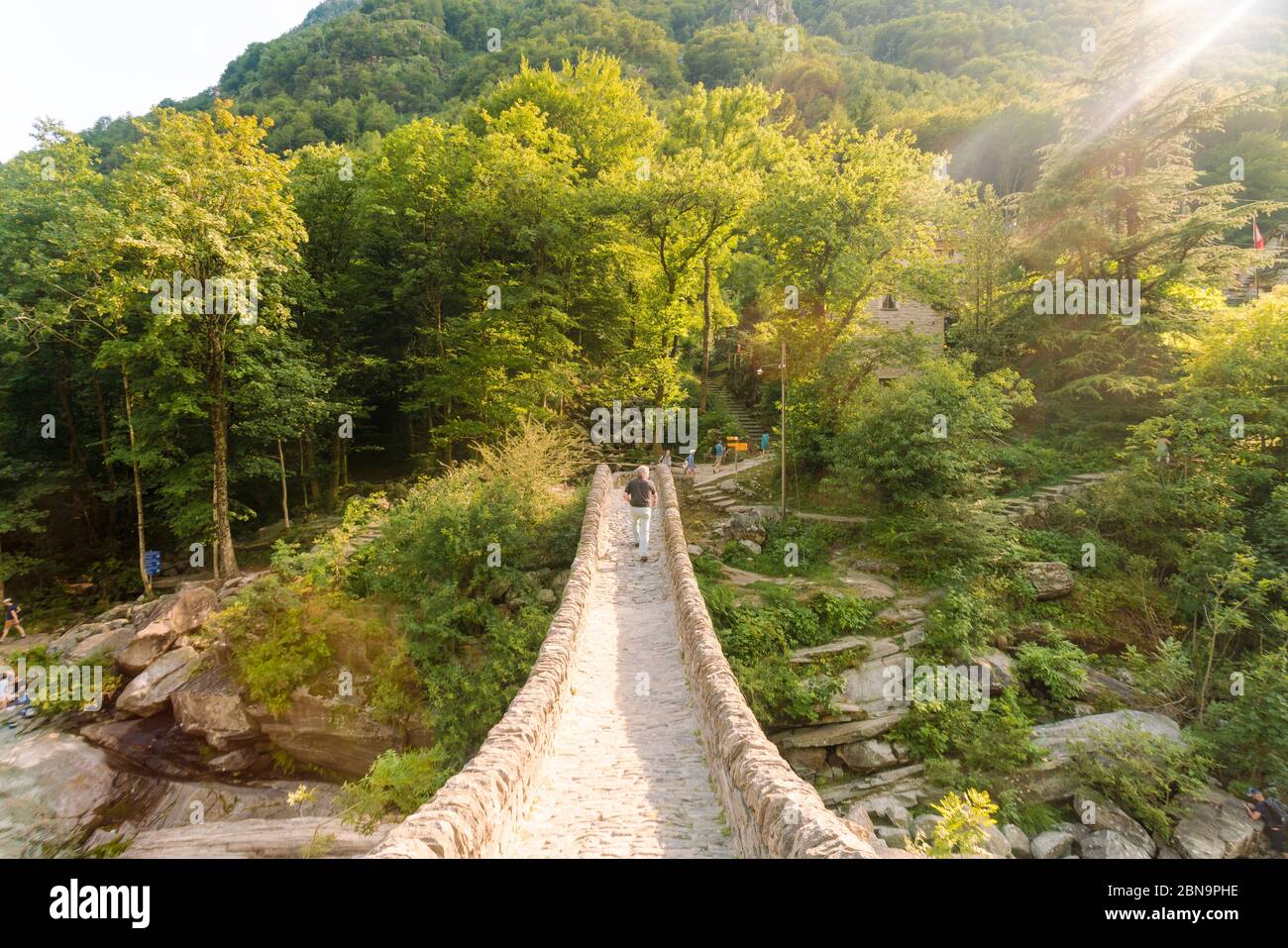Uomo che attraversa il ponte medievale della verzasca 'Ponte dei salti' Foto Stock