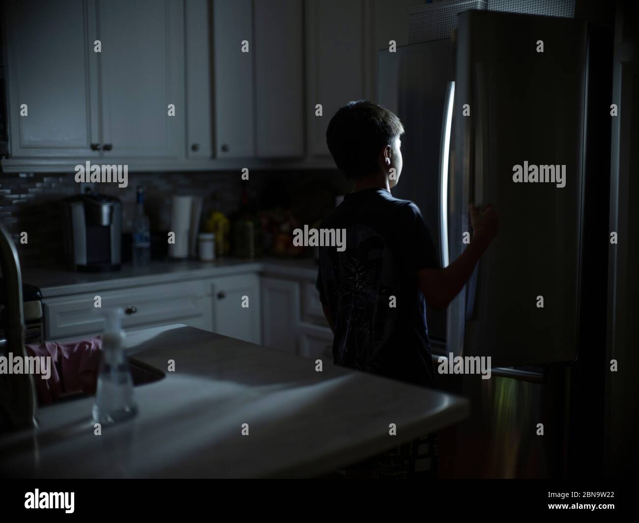 Un ragazzo di 12 anni cerca uno spuntino notturno nel frigorifero Foto Stock