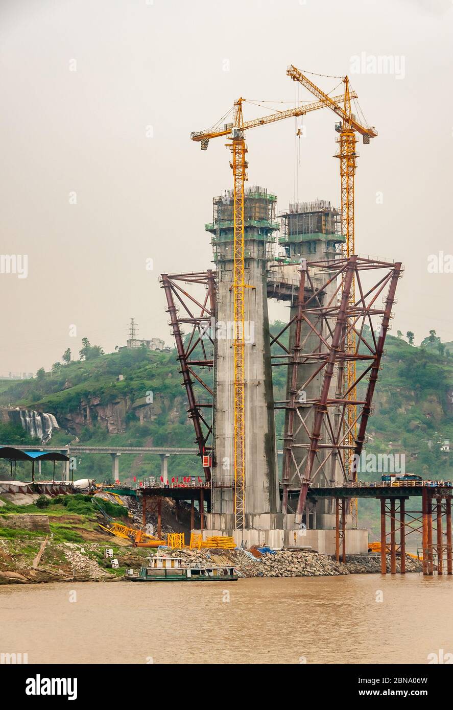 Fengdu, Chongqing, Cina - 8 maggio 2010: Fiume Yangtze. Primo piano di torre di sospensione in calcestruzzo per ponte in costruzione con 2 alte gru gialle ov Foto Stock