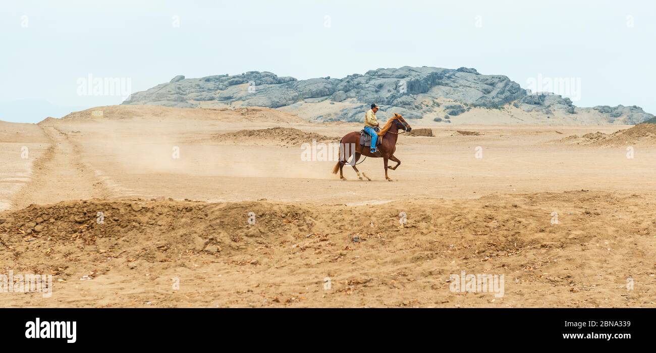 Un uomo peruviano anziano che cavalcano un cavallo passo nel deserto di sabbia del nord del Perù vicino Trujillo. Foto Stock