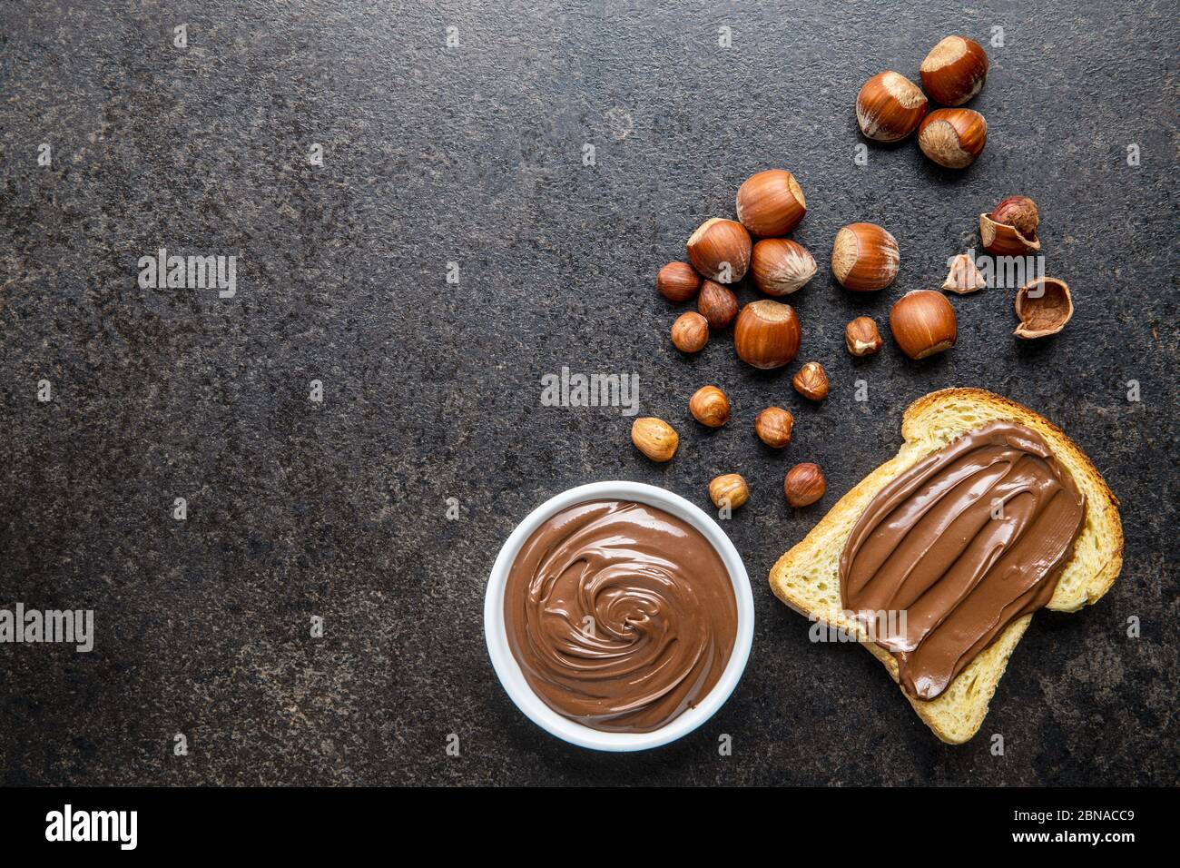 Tostare il pane con la nocciola spalmata. Crema di cioccolato dolce su tavolo da cucina nero. Vista dall'alto. Foto Stock