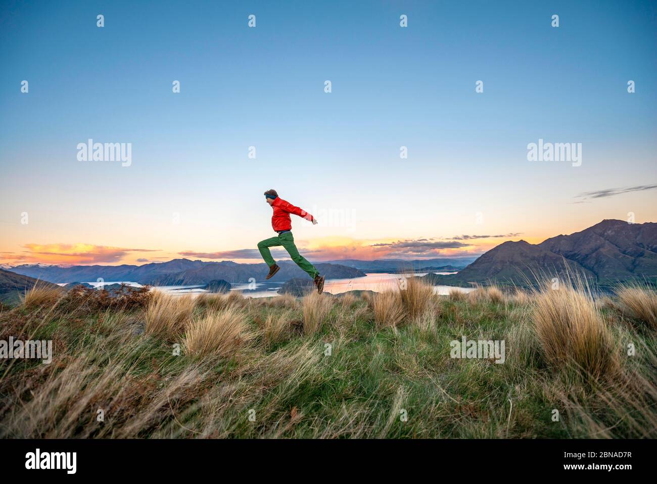 Gli escursionisti salta in aria, vista panoramica del lago Wanaka e delle montagne al tramonto, Rocky Peak, Glendhu Bay, Otago, South Island Foto Stock