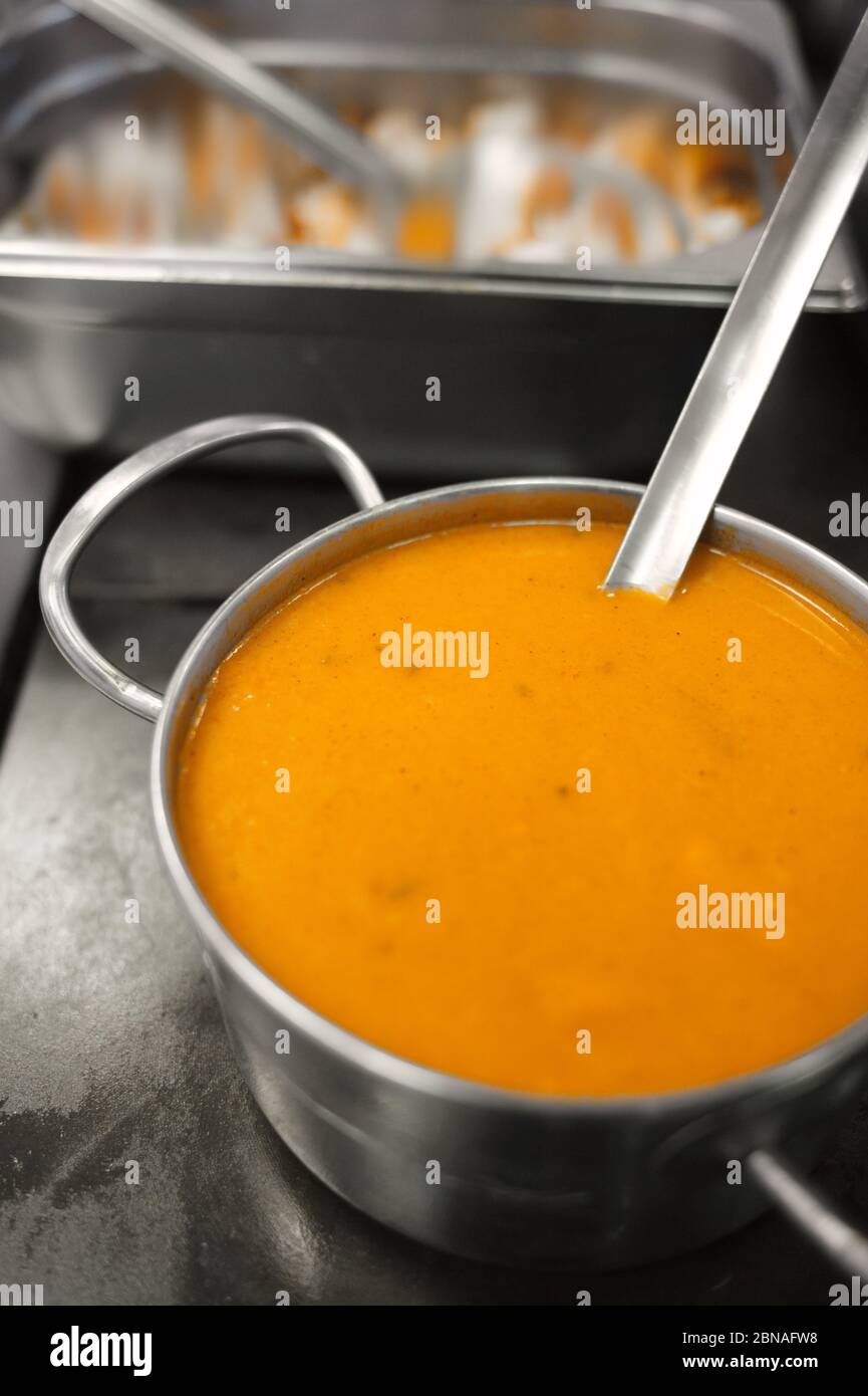 Zuppa gialla in un recipiente di metallo. Preparazione del pranzo nella sala da pranzo. Stufato esotico. Cibo in una piastra di acciaio. Foto Stock