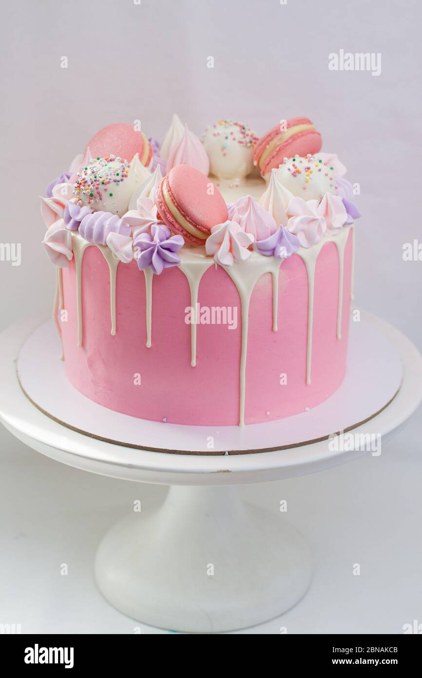 Dolce rosa decorato con cioccolato bianco fuso, macaroon, meringhe, torte pop e caramelle su cakestand bianco. Sfondo semplice. Foto Stock