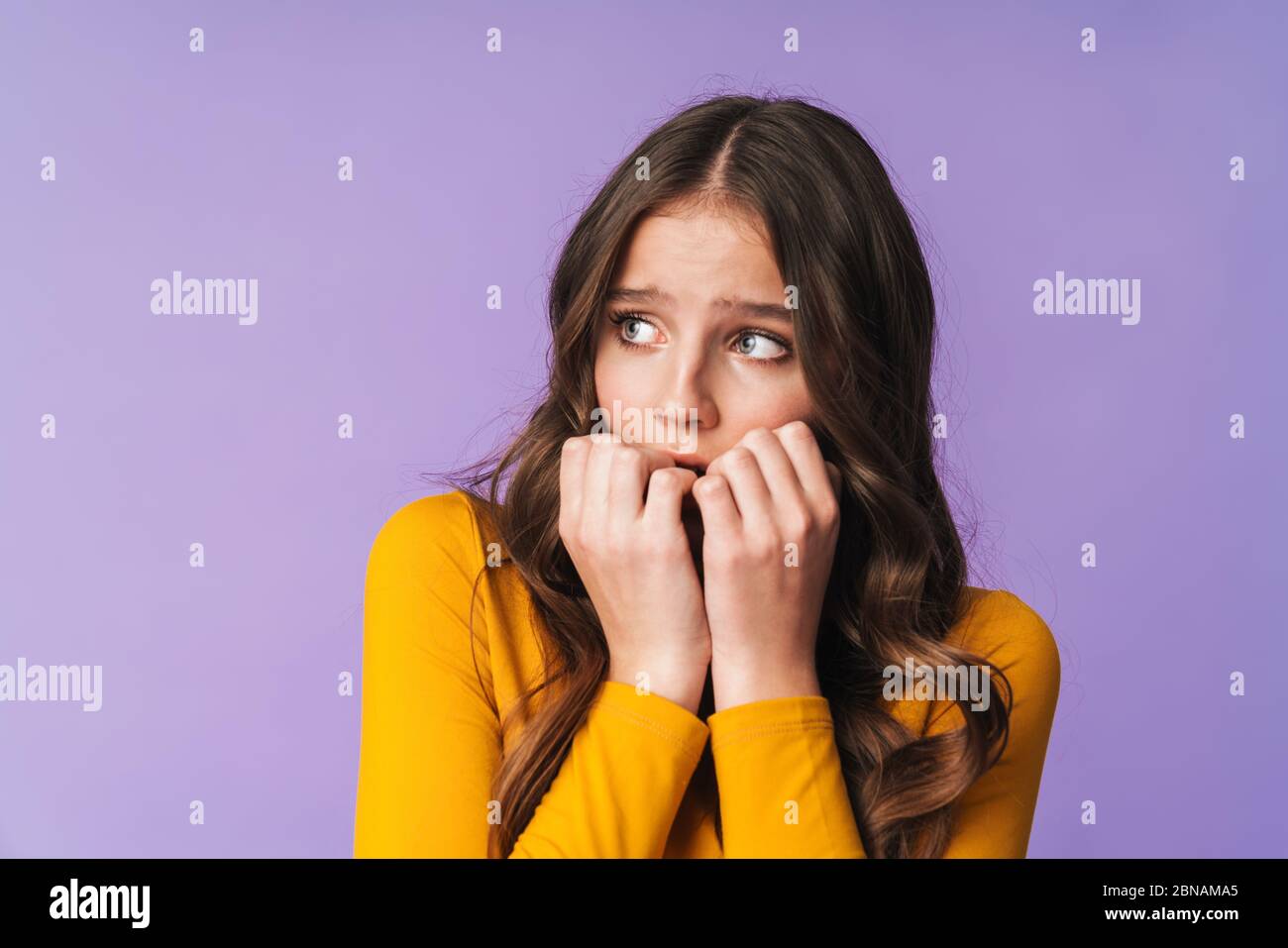 Immagine di giovane donna dispiaciuta con lunghi capelli marroni spaventati e mordenti le sue unghie isolate su sfondo viola Foto Stock