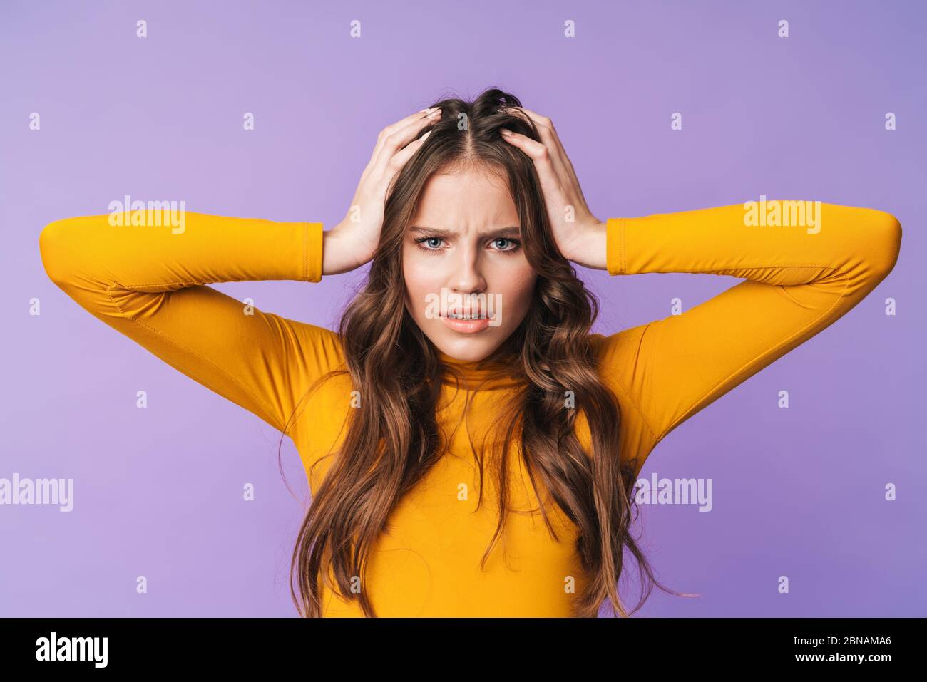 Immagine di giovane donna dispiaciuto con lunghi capelli marroni nervosi e afferrare la testa isolata su sfondo viola Foto Stock