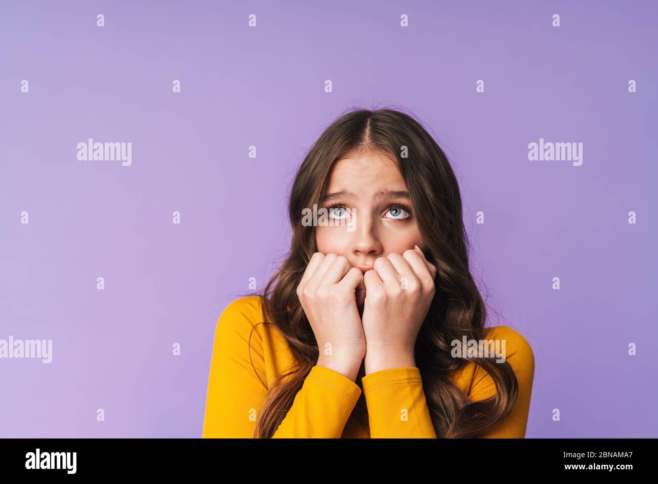 Immagine di giovane donna dispiaciuta con lunghi capelli marroni spaventati e mordenti le sue unghie isolate su sfondo viola Foto Stock