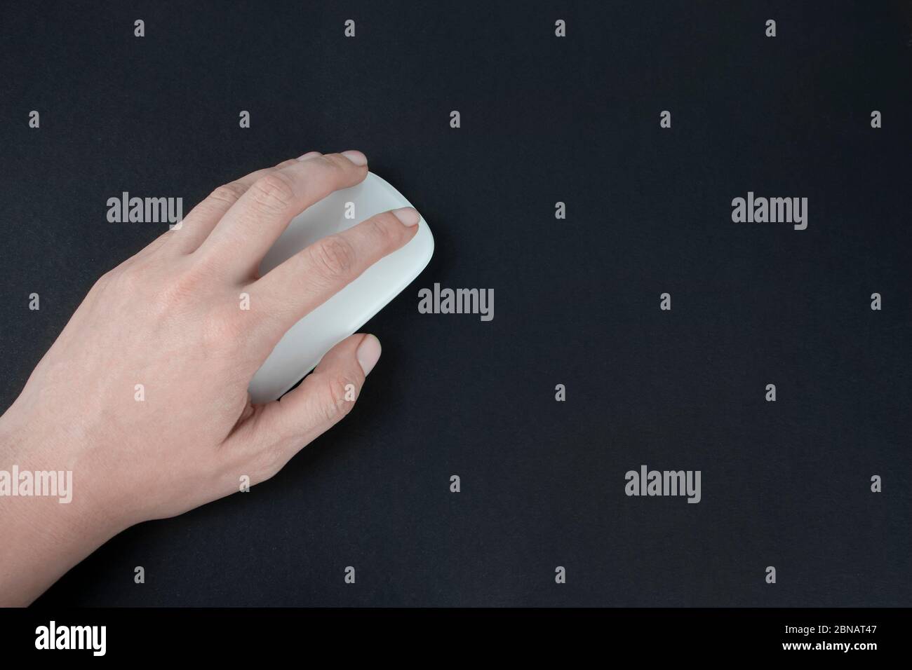 Donna caucasica mancina che usa il mouse del computer. Mano femmina che tiene il mouse del computer su sfondo nero scuro. Foto Stock