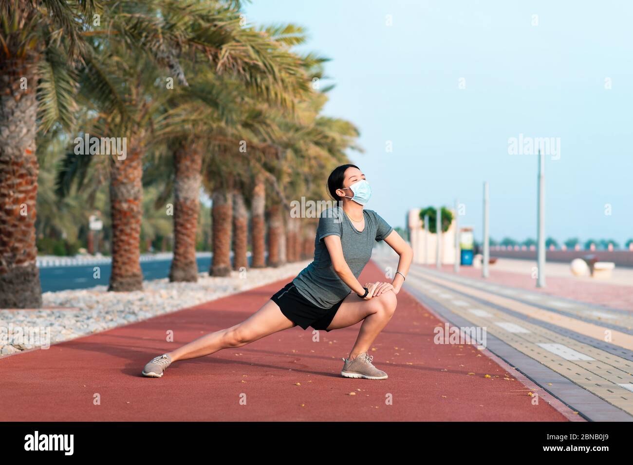 Donna asiatica che si esercita e si stretching mentre indossa una maschera chirurgica protettiva per riscaldarsi prima di allenamento fitness all'aperto Foto Stock