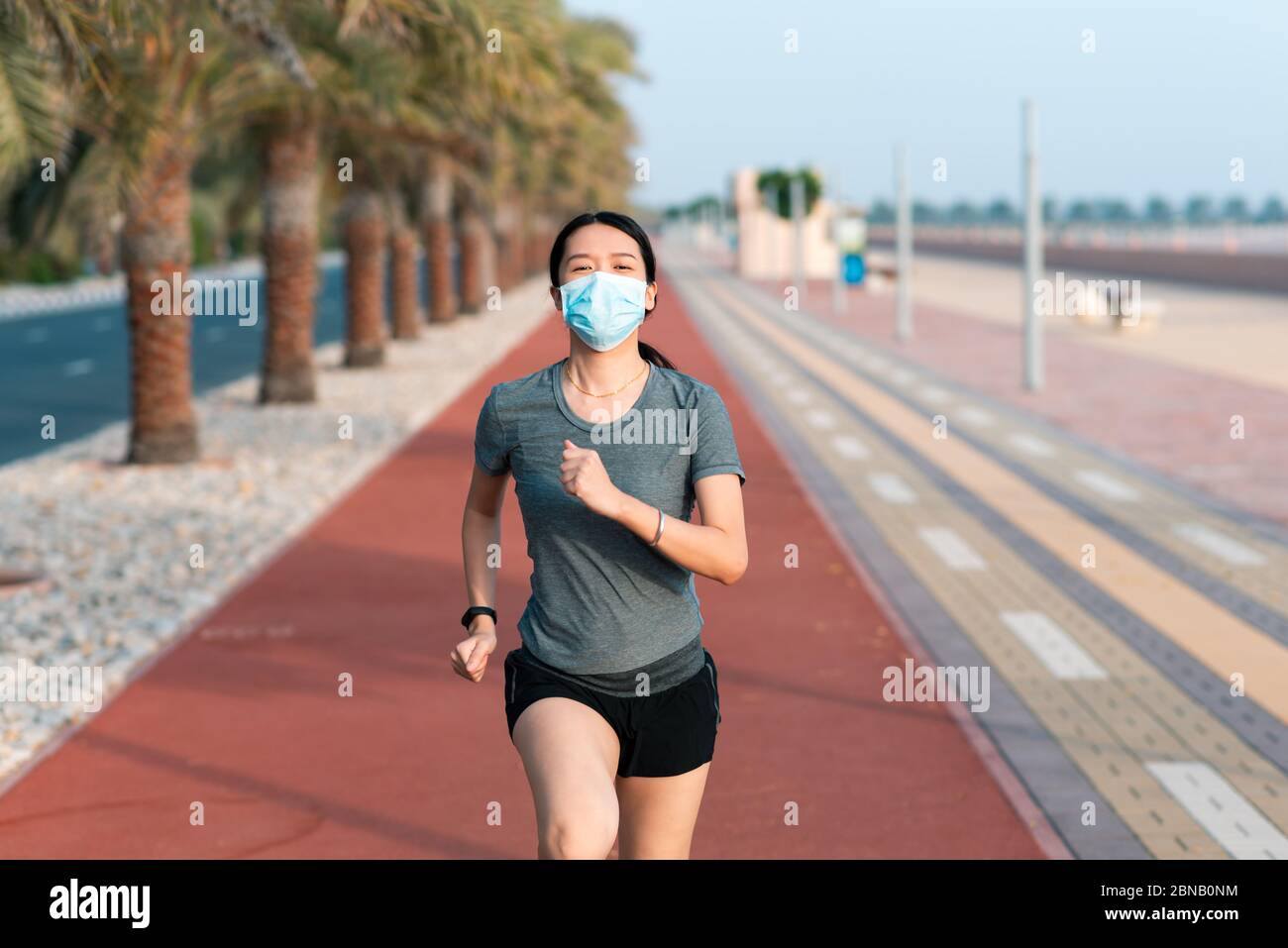 Donna asiatica che fa jogging sulla pista da corsa indossando una maschera chirurgica protettiva per prevenire la diffusione del coronavirus e rimanere al sicuro Foto Stock