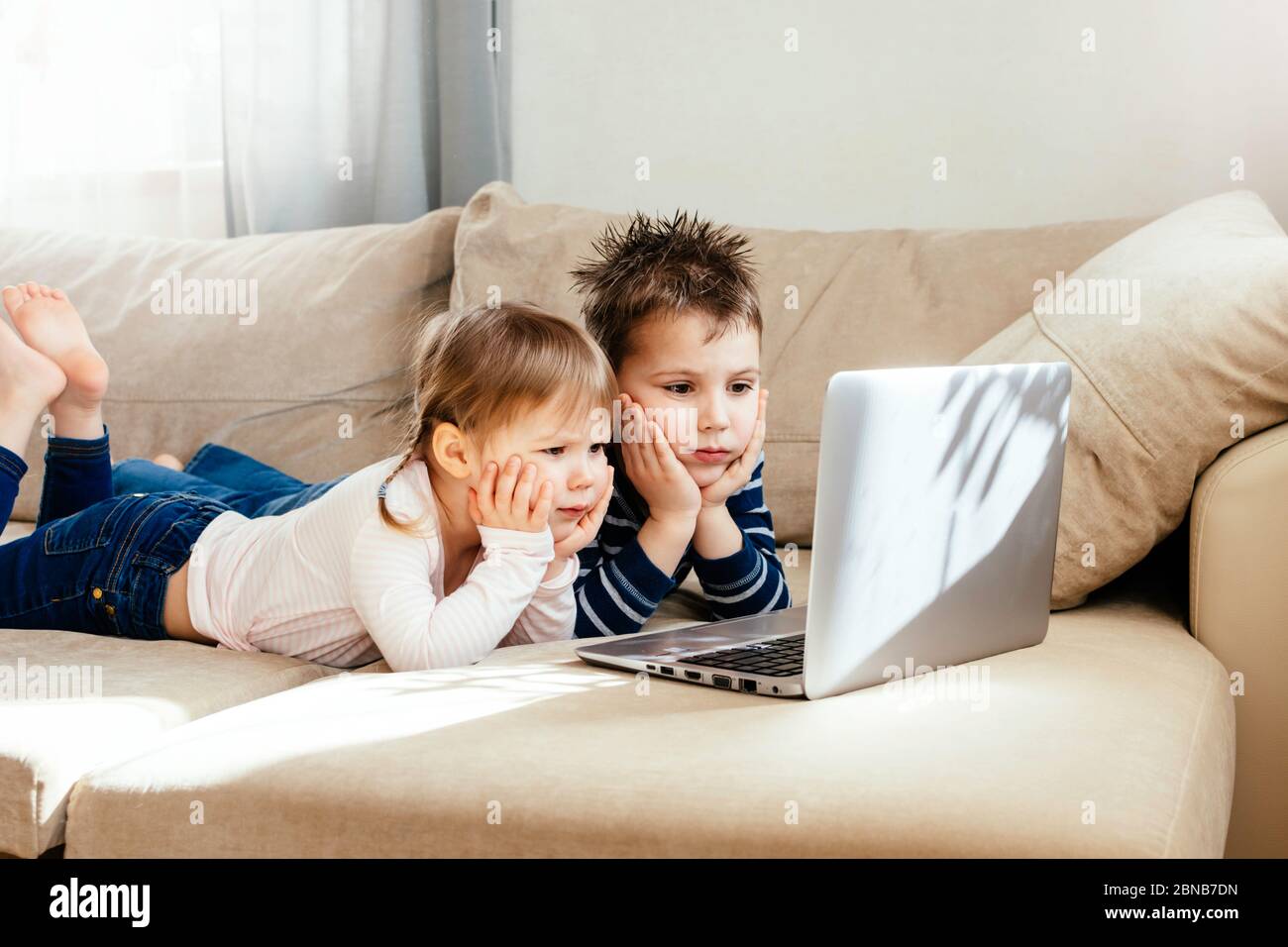 I bambini studiano a casa utilizzando lezioni online sul divano, guardando cartoni animati online. Quarantena a casa. Formazione a distanza, formazione online. Foto Stock