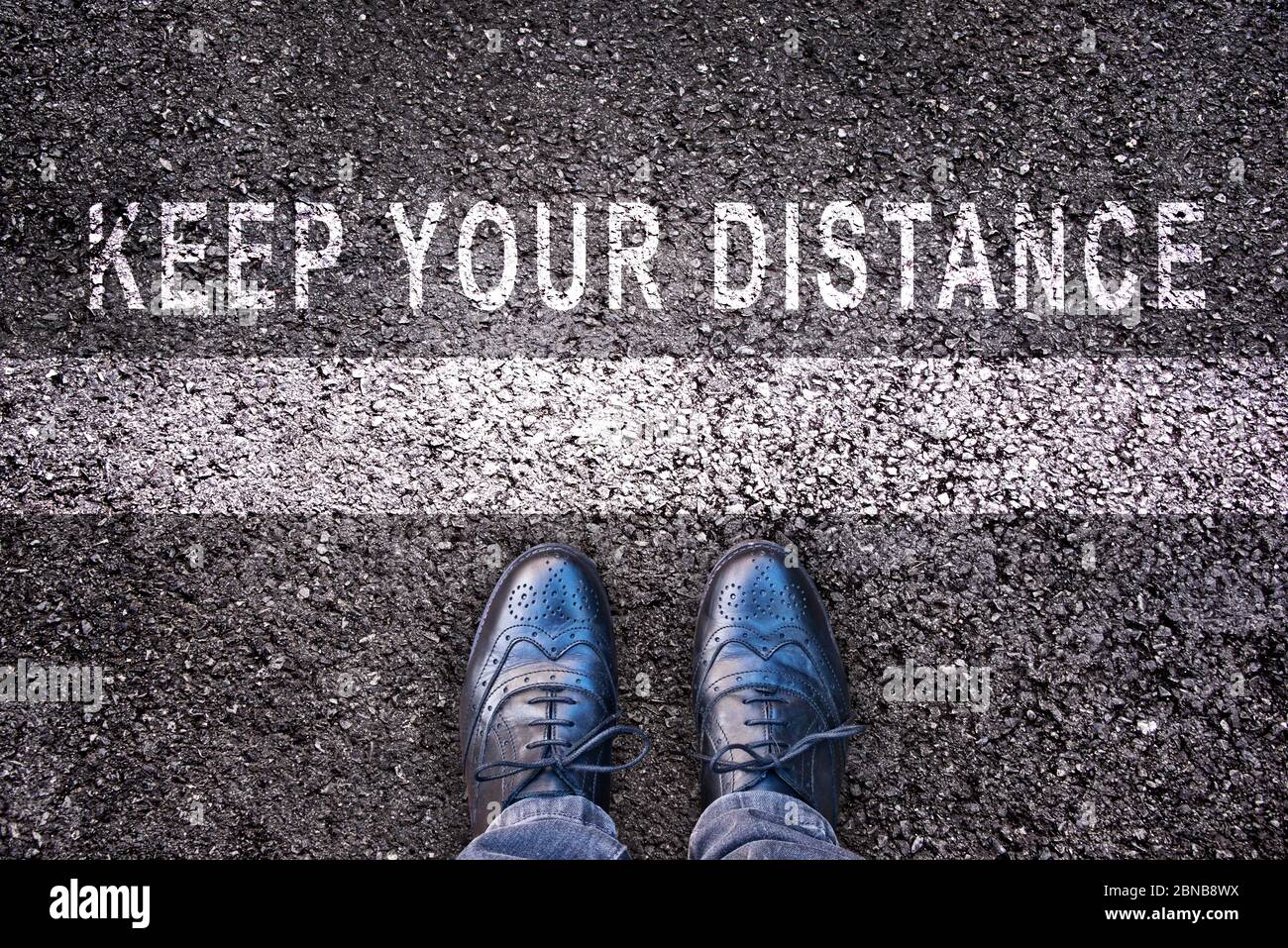 Scarpe con messaggio 'mantenere la distanza' scritto su asfalto Foto Stock
