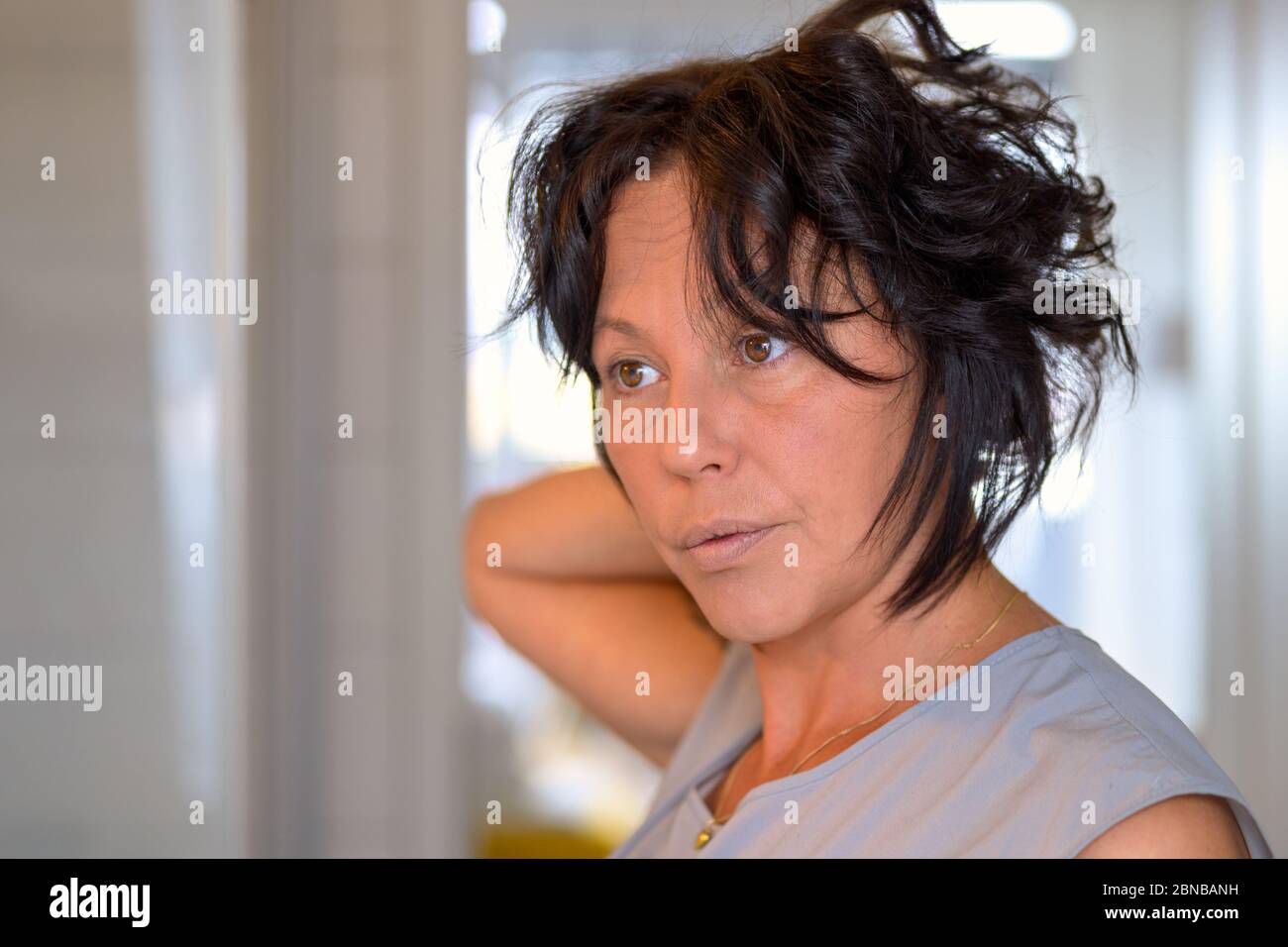 Donna ispanica con capelli scuri e mousled in piedi in interni guardando da parte con un'espressione premurosa Foto Stock