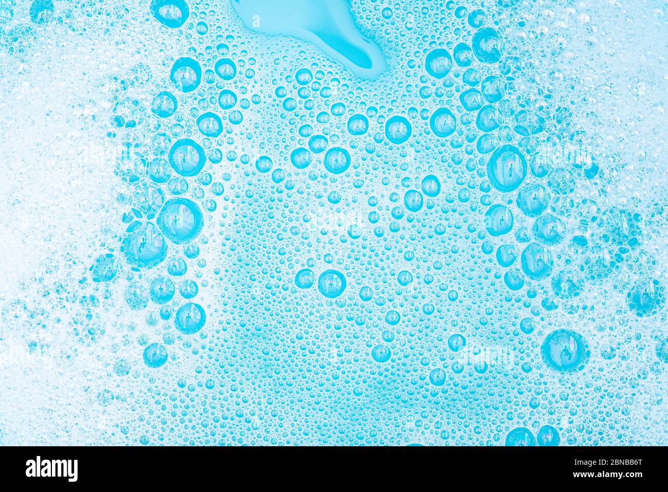 Primo piano schiuma bianca con bolle sulla superficie dell'acqua, polvere di lavaggio con sapone e bagno blu, fondo astratto bolla trasparente. Foto Stock