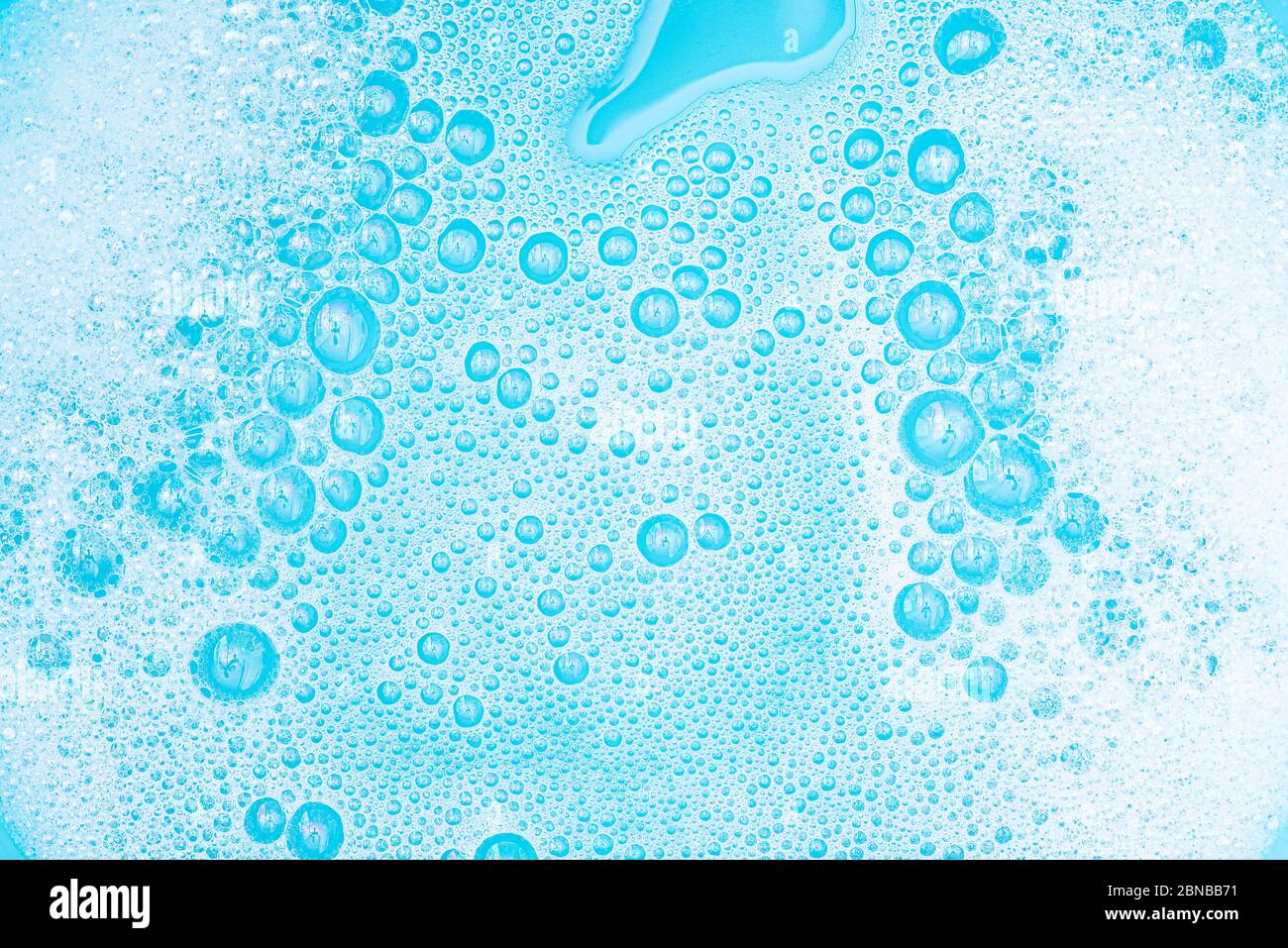 Primo piano schiuma bianca con bolle sulla superficie dell'acqua, polvere di lavaggio con sapone e bagno blu, fondo astratto bolla trasparente. Foto Stock