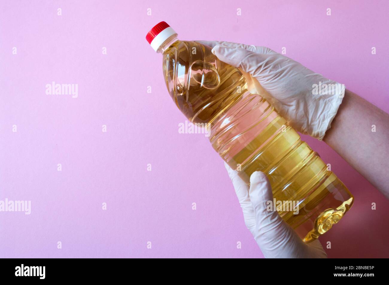 Le mani trattengono olio di girasole puro in una bottiglia di plastica. Condimento per insalate. Su sfondo rosa. Foto Stock