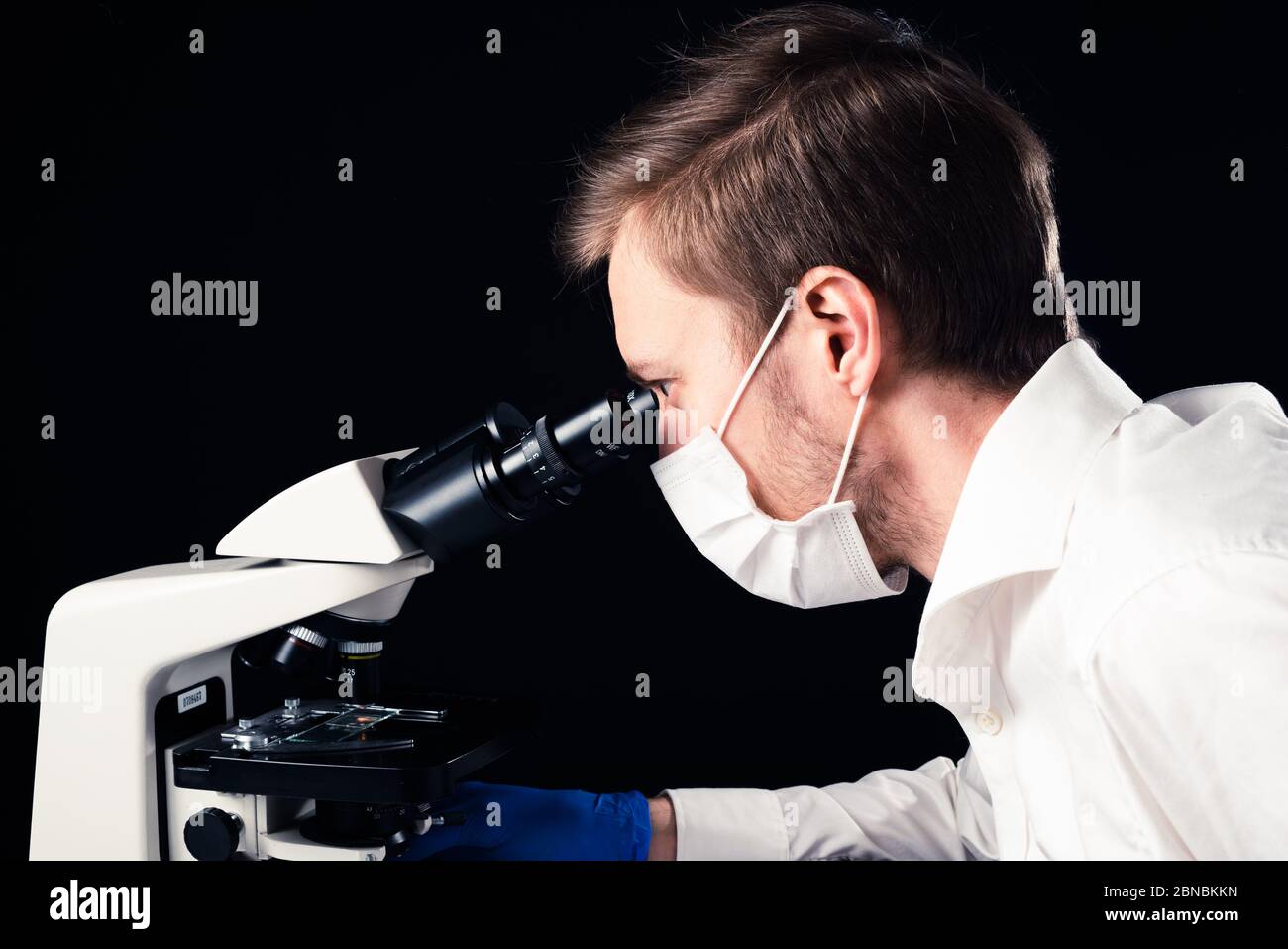 Bianco scienziato maschile con microscopio binoculare, indossare maschera e guanti. Foto Stock