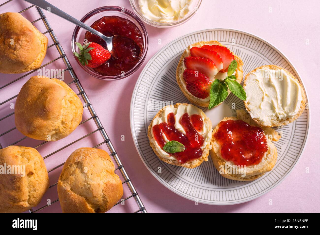 Gustosa colazione di focaccine con crema coagulata e marmellata di fragole su sfondo rosa, vista dall'alto Foto Stock