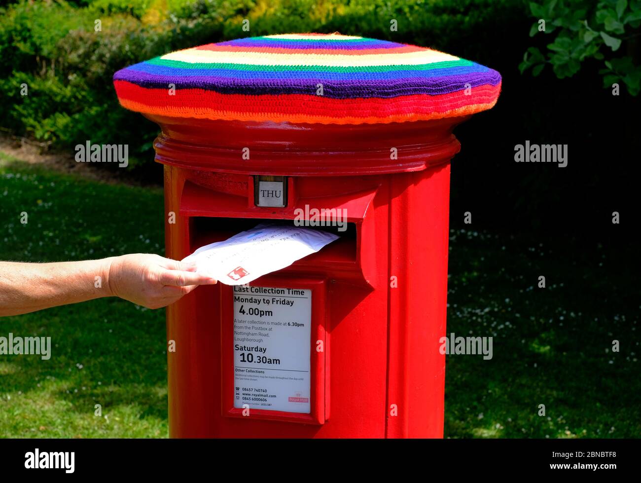 Loughborough, Leicestershire, Regno Unito. 14 maggio 2020. Una donna invia una lettera in una casella postale Royal Mail che è stata bombata in filo di colori arcobaleno per mostrare il sostegno per i lavoratori chiave durante il blocco pandemico coronavirus. Credit Darren Staples/Alamy Live News. Foto Stock