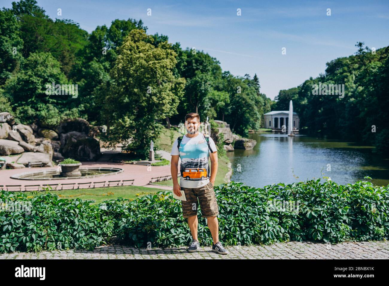 Sofia Park, Ucraina. Bell'uomo con barba in un parco dendrologico. Uomo con uno zaino sullo sfondo del lago con una fontana e un bianco Foto Stock