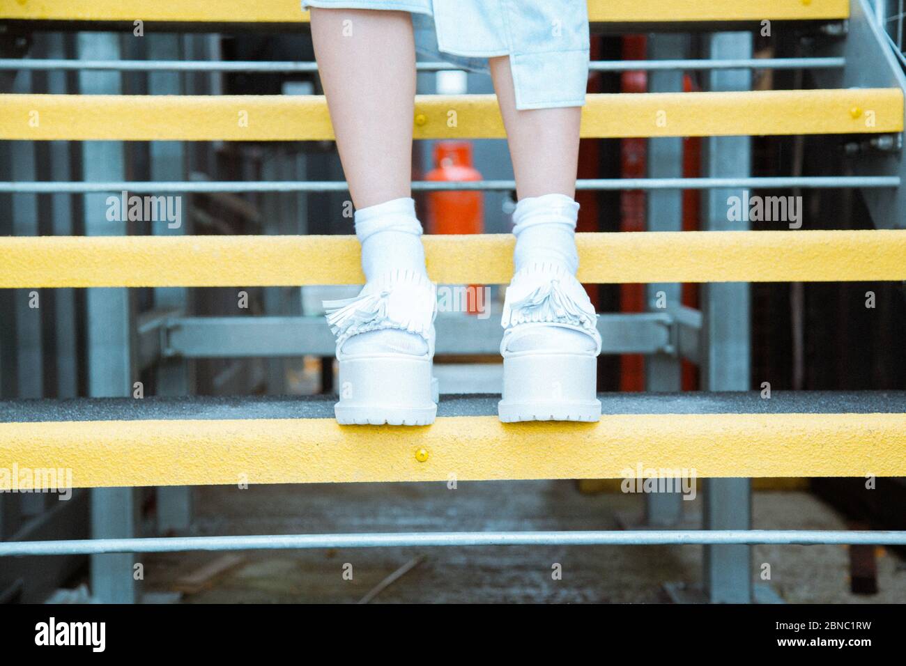 Persona che indossa scarpe bianche in piedi su gradini gialli con un sfondo sfocato Foto Stock