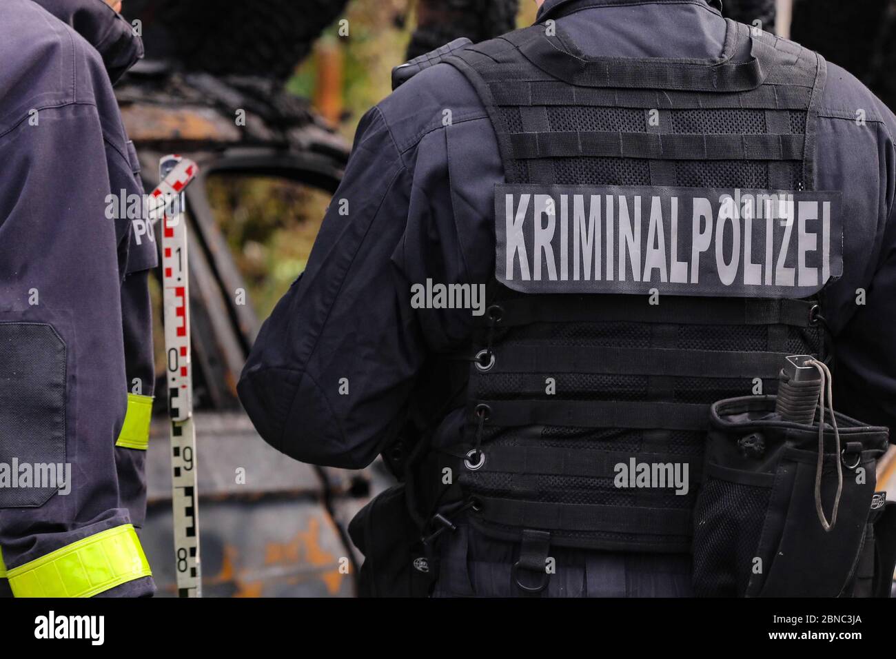 Dresda, Germania. 13 maggio 2020. L'investigatore della causa dell'incendio con l'iscrizione 'Kriminalpolizei' sulla schiena è in un taglio sul lato destro del quadro. Al centro dell'immagine è visibile un bastoncino di misurazione. Sul lato sinistro della sfocatura è un altro ufficiale nel taglio. Nella sfocatura sullo sfondo dell'immagine, il veicolo distrutto è visibile. Credit: Tino Plunert/dpa-Zentralbild/ZB/dpa/Alamy Live News Foto Stock