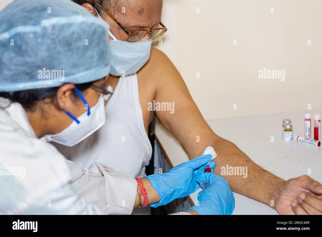 Nurse prende il campione di sangue di un maschio indiano anziano per l'esame del sangue medico alla luce della pandemia di coronavirus Foto Stock