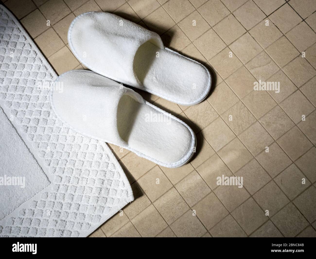 Asciugamani bianchi e paio di pantofole bianche su fondo in ceramica. Concetto di spa Foto Stock