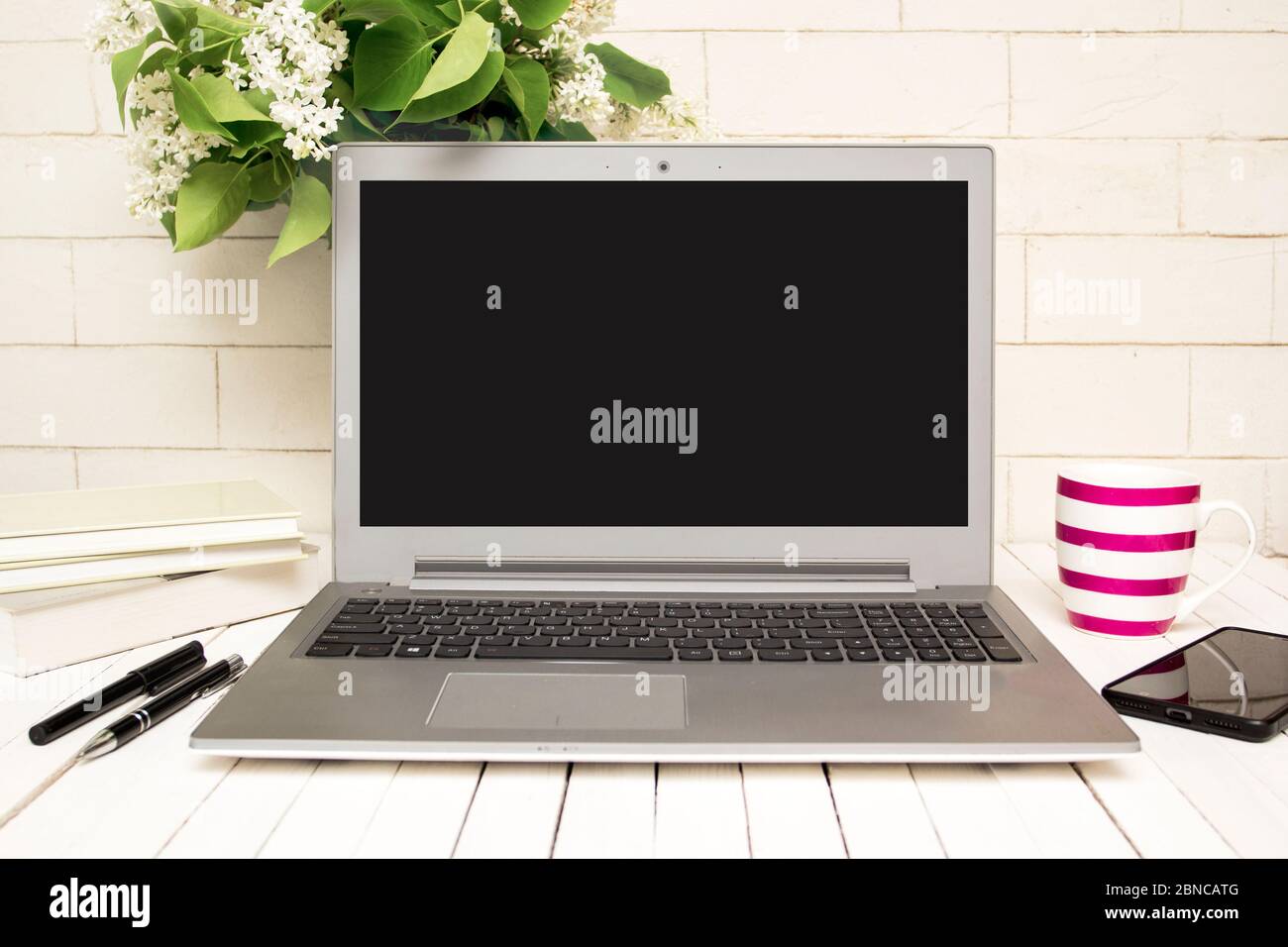 Moderna scrivania da ufficio con computer portatile, smartphone, libri, tazza di caffè e fiori Foto Stock