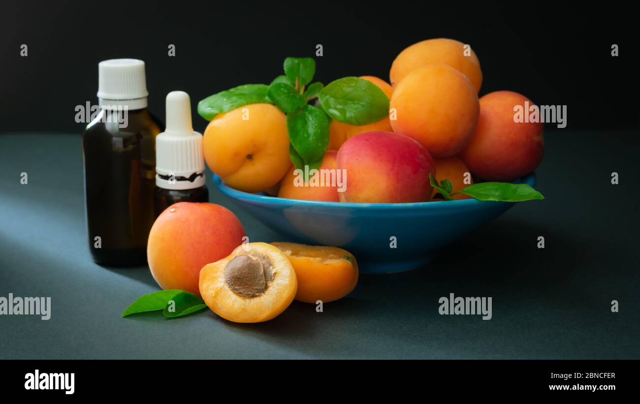 il concetto di cosmetici naturali, albicocche con bottiglie di vetro con olio su fondo scuro Foto Stock