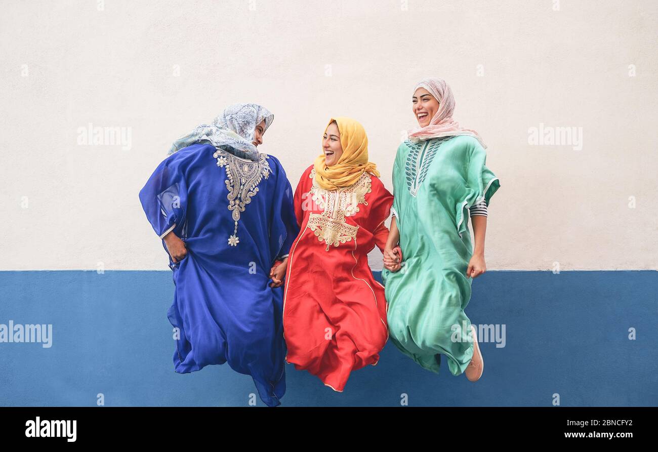 Donne musulmane felici che hanno divertimento saltando e ridendo insieme all'aperto - stile di vita della gente e concetto di religione di cultura - sfondo bianco e blu Foto Stock