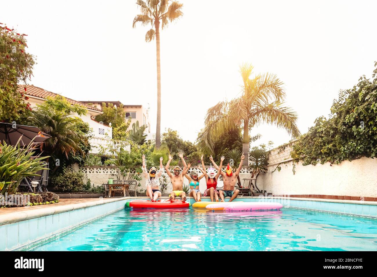 Gruppo amici felici che indossano maschera facendo festa in piscina - giovani che si divertono festeggiando evento in esclusiva piscina estate vacanza tropicale Foto Stock