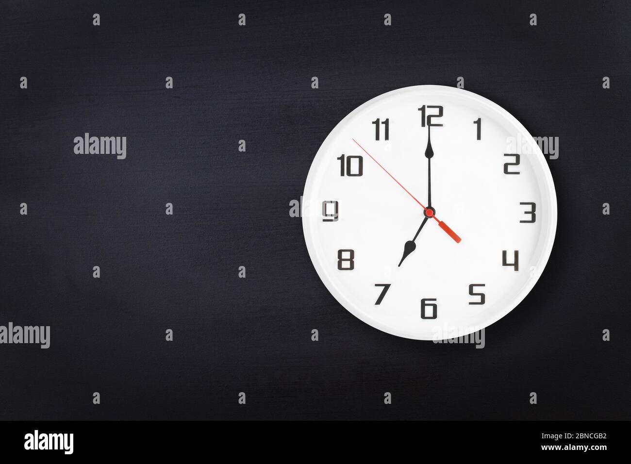 Orologio da parete bianco su sfondo nero della lavagna. dalle 7:00 alle 19:00 Foto Stock