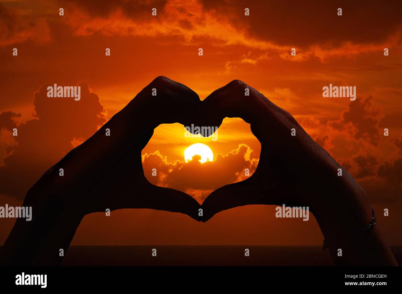 Le mani modellano un cuore prima di un tramonto Foto Stock