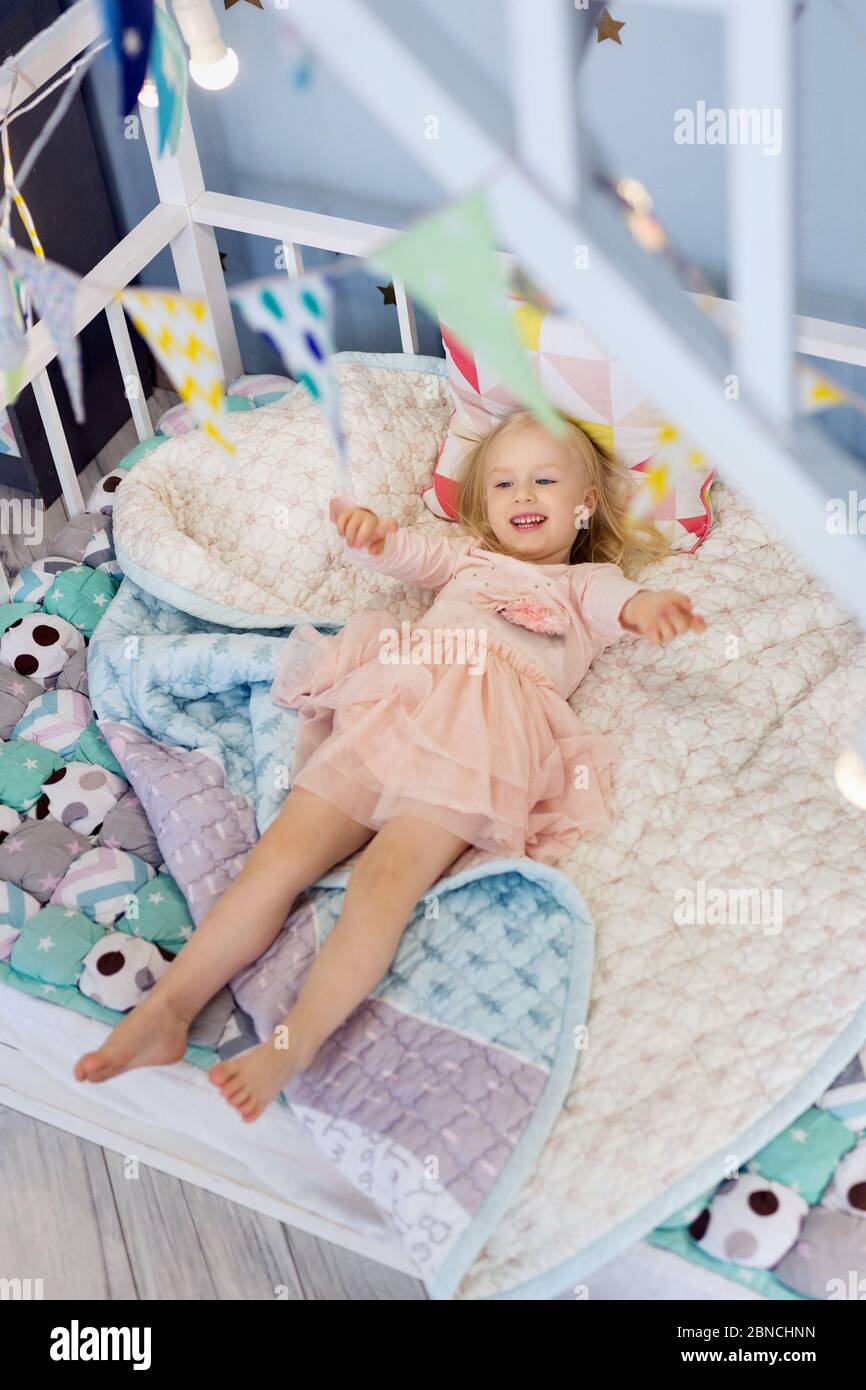 Ragazza felice che indossa un vestito carino sdraiato su un letto accogliente decorato Foto Stock