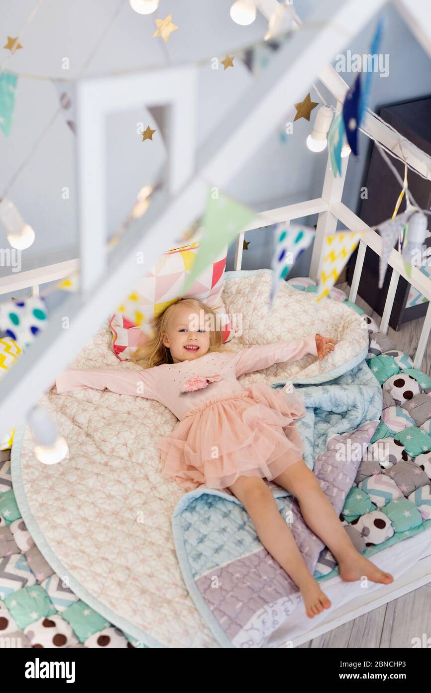 Felice 3 anni adorabile ragazza sdraiata sul letto decorata con lampadine Foto Stock
