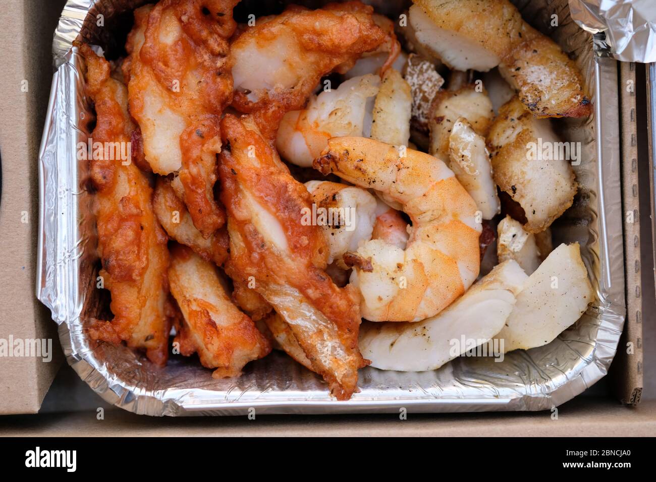 Fette di gamberetti e pesce in un contenitore di alluminio. Pesce merluzzo in pastella e gamberi re vista dall'alto. Pasto con consegna a domicilio e pesce. Foto Stock