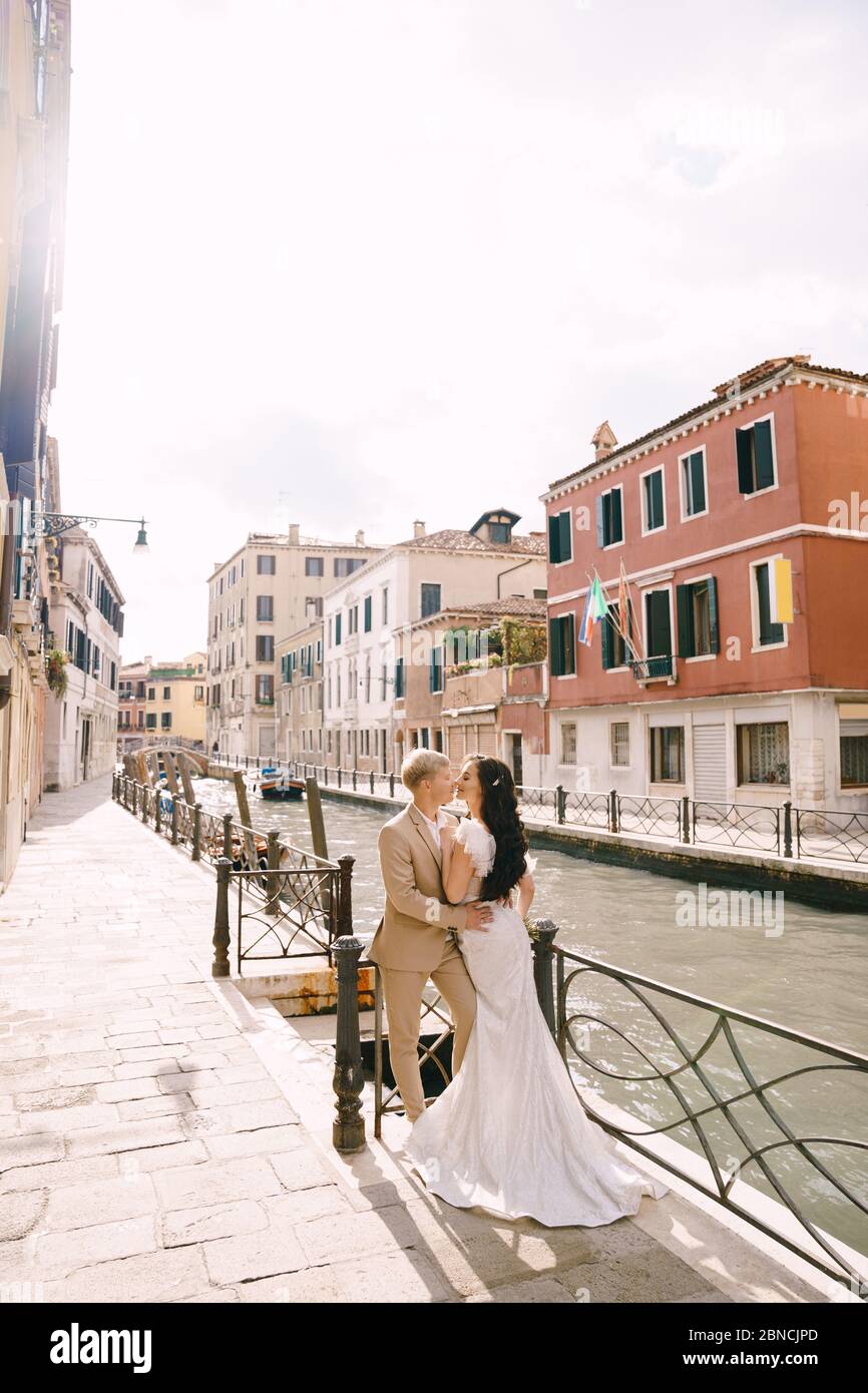 Matrimonio in Italia a Venezia. Sposi sposi si abbracciano sulle rive del  canale di Venezia. Lo sposo abbraccia la sposa dalla vita. Abito da sposa  bianco con Foto stock - Alamy