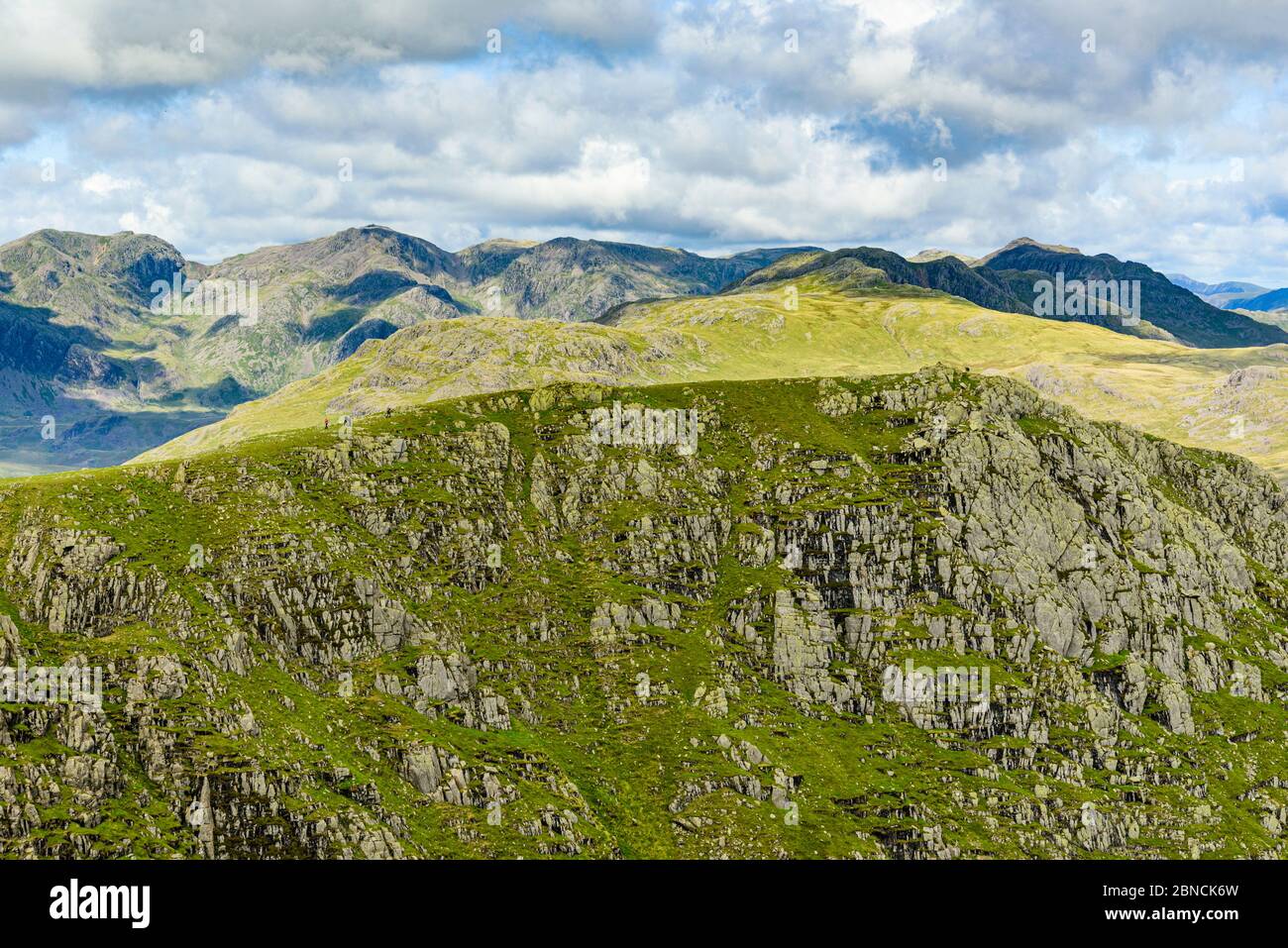 Vista da Swirl come con gli escursionisti su grandi Carrs nel Coniston Fells, Lake District, con Scafell, Scafell Pike, Crinkle Crags e Bowfell dietro Foto Stock