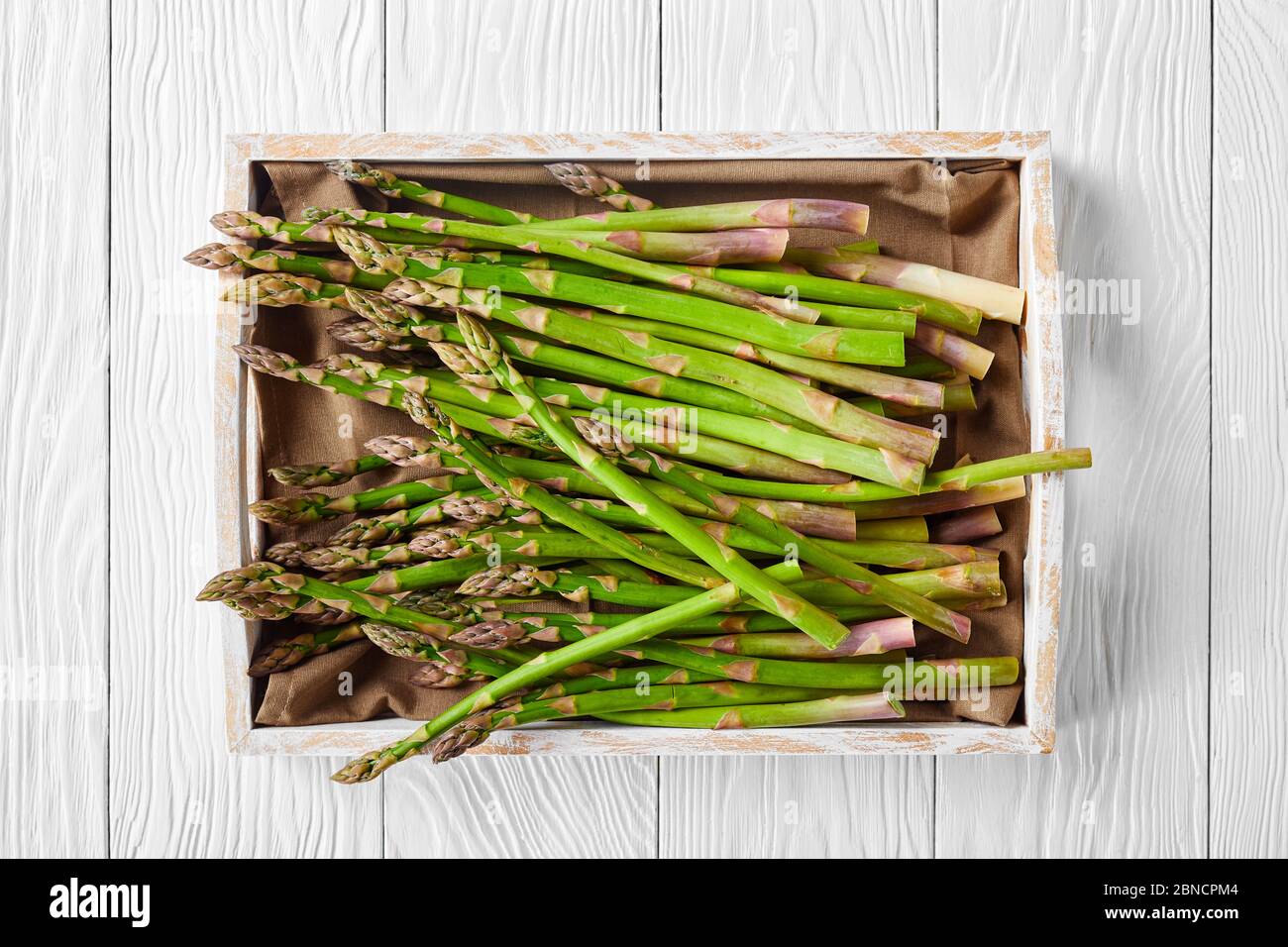 primo piano di asparagi verdi freschi non cotti in una scatola rustica di legno su un tavolo di legno bianco, piatto Foto Stock