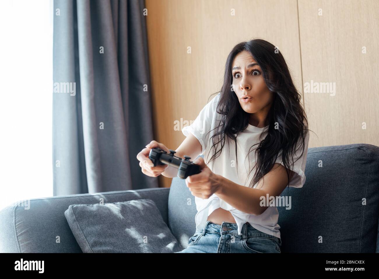 KIEV, UCRAINA - 9 APRILE 2020: Ragazza sorpresa giocando video gioco con joystick su auto isolamento Foto Stock